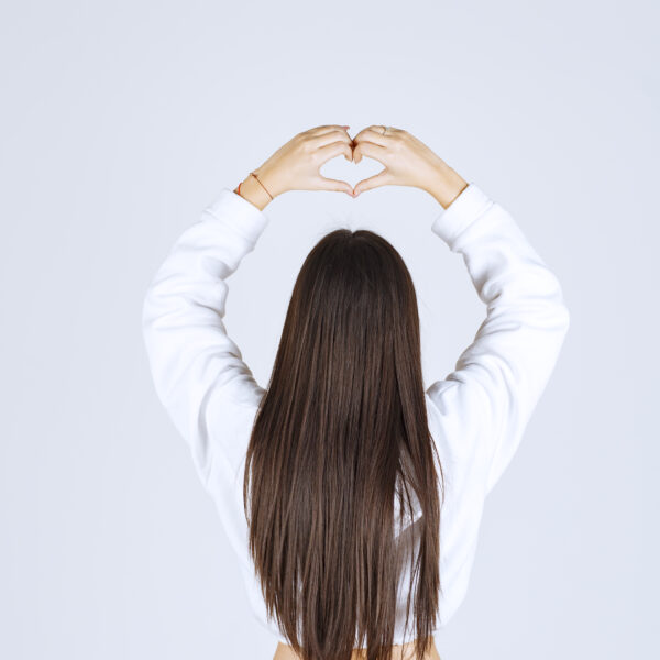 Photo of a young girl in white hoodie showing heart with two hands. High quality photo